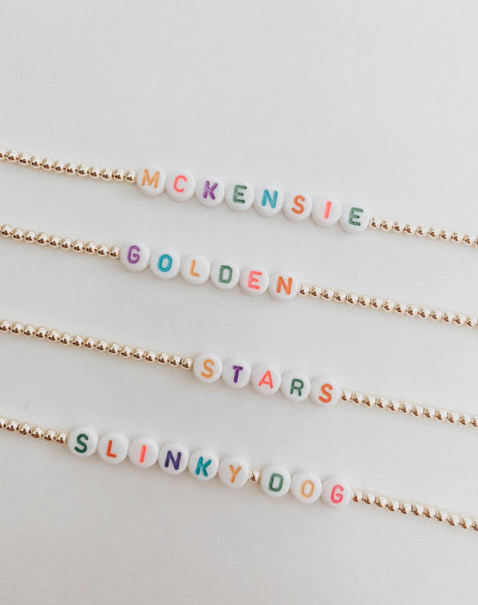 these bracelets are small gold beads with white beads that have different color letters that are able to spell out whatever you decide.