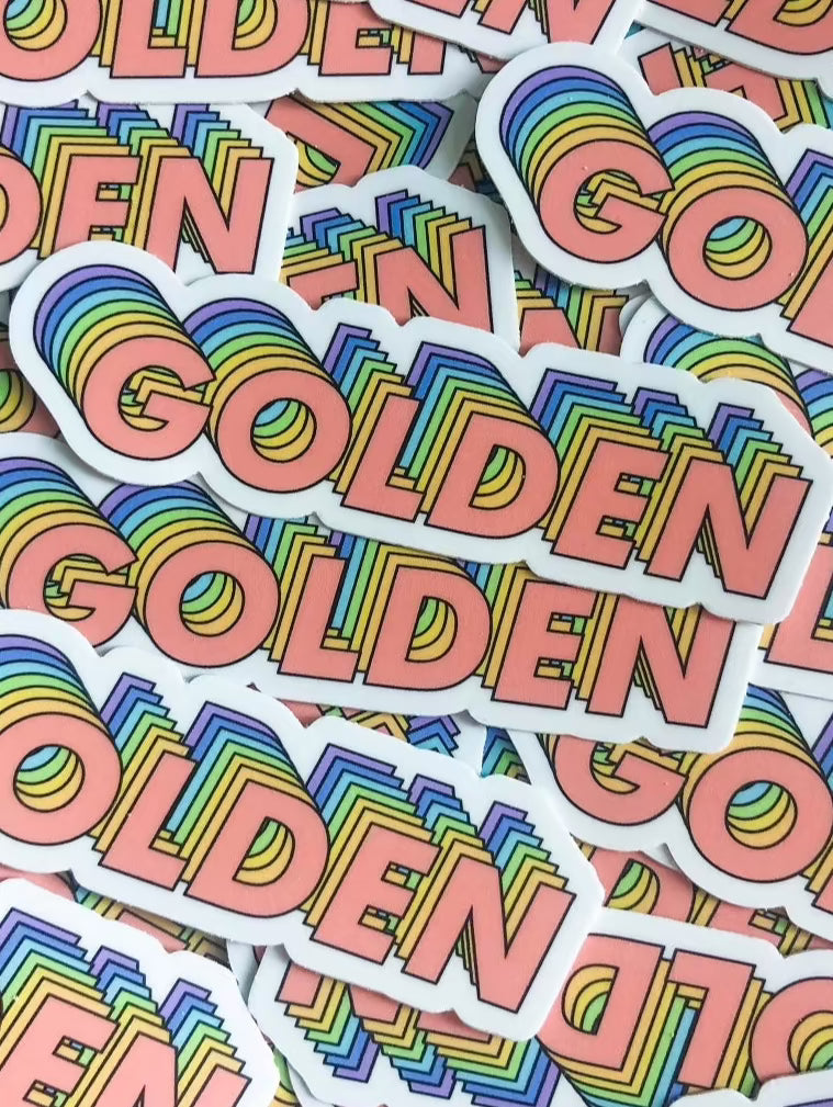 This sticker has the world golden on it in all caps. The sticker is cut so that it indents around where the letters curve. The text is layered with different colors. The first color in the front is pink, then orange, yellow, green, blue and purple.